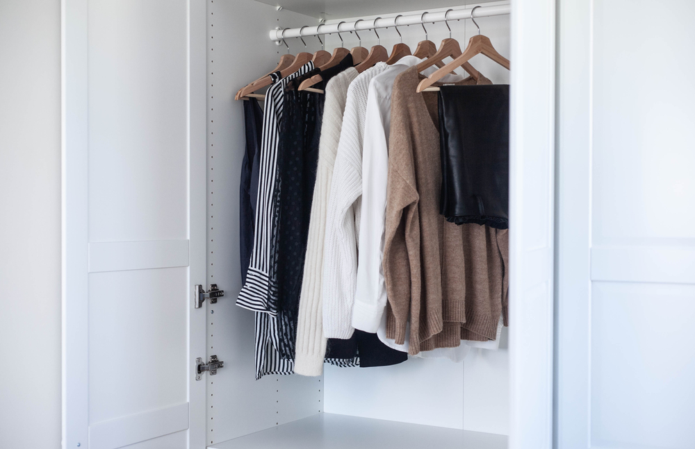 A minimalist capsule wardrobe featuring neutral-colored blazers, denim jeans, and a white shirt hanging on a clothing rack.
