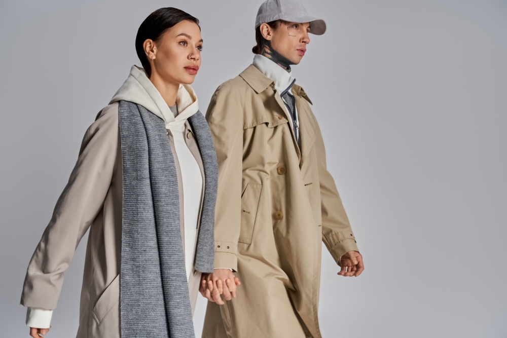 A stylish man and woman wearing a trench coat over a sweater and Tshirt, perfect for fall and winter.