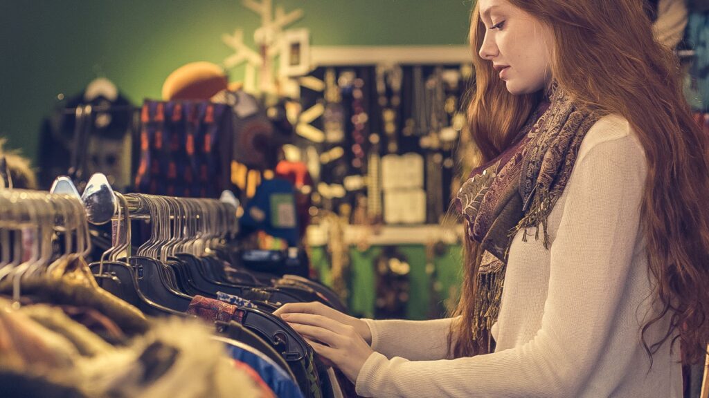 Woman browsing thrift store racks to find unique clothing pieces.